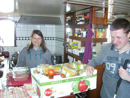 Foto: Katrin und Norbert in der K�che. Auf der Theke steht eine gro�e Kiste mit allen Lebensmitteln f�r das Mittagessen (23 Personen). Beie l�cheln. Liegt es vielleicht daran, weil die Kiste so gro� ist, oder weil sie sich schon auf das essen freuen "g"?