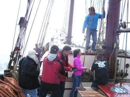 Das erste Segel wird gesetzt. Bootsmann Jan erklärt die ersten Arbeiten. Alle Teilnehmer haben das Seil zum segelsetzen in den Händen.